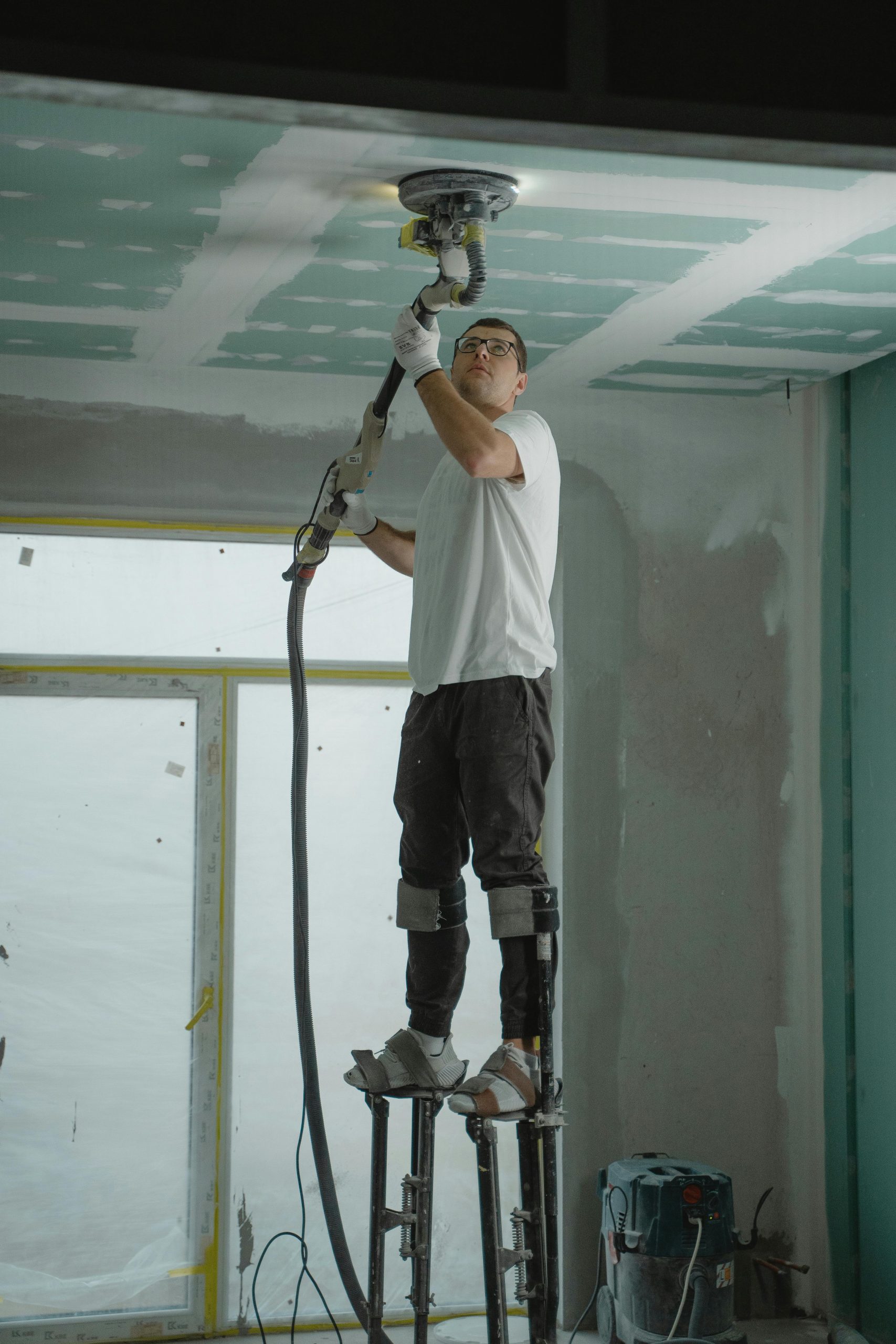 Construction worker smoothing a wall indoors using safety gear.